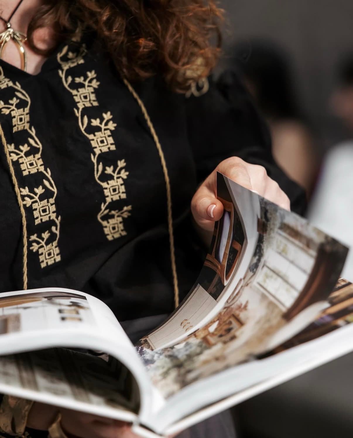 Gros plan d’une blouse brodée et de mains qui feuillettent un livre de décoration