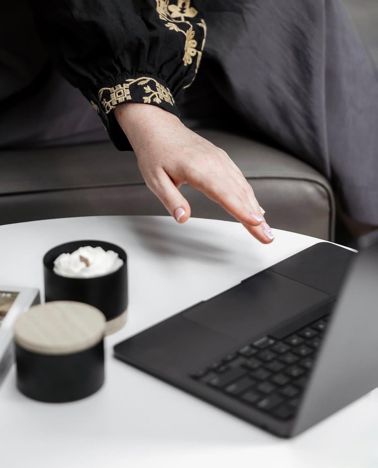 La main d’Anna, en manche brodée, tendue vers un ordinateur portable sur une table blanche avec des bougies