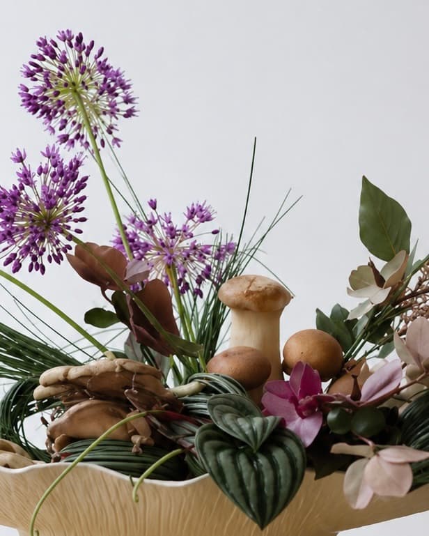 Floral arrangement with purple allium, mushrooms and leaves in a ceramic bowl