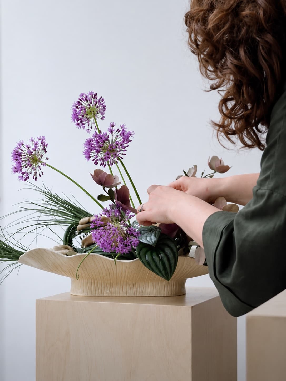 Anna's hands arranging allium and leaves in a ceramic bowl