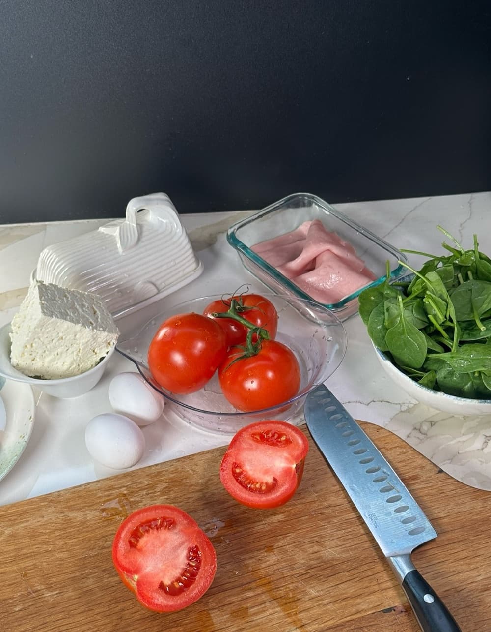 Food content shoot: tomatoes, feta, spinach and eggs on a marble counter